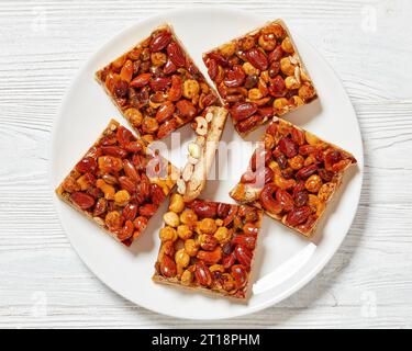 barres sablées de caramel mélangées aux noix maison sur une plaque blanche sur une table en bois blanc, vue horizontale d'en haut, pose à plat, gros plan Banque D'Images