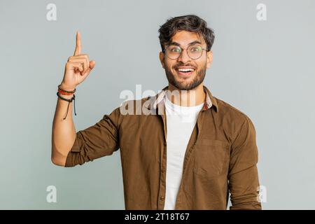Eureka. Inspiré jeune homme indien pointant du doigt vers le haut avec la bouche ouverte, ayant une bonne idée, plan, démarrage, montrant l'inspiration geste de motivation, solution de problème. Gars arabe isolé sur fond gris Banque D'Images