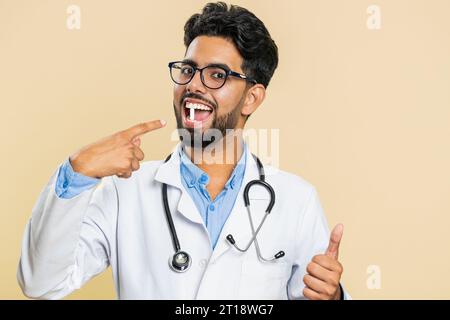 Sourire indien docteur homme hindou met de pilule de comprimé capsule blanche dans la bouche, recommande le traitement de cure d'immunisation de médicaments. Les soins de santé. Vitamines pour les articulations, les cheveux, la peau, les ongles. Pharmacien apothicaire Banque D'Images