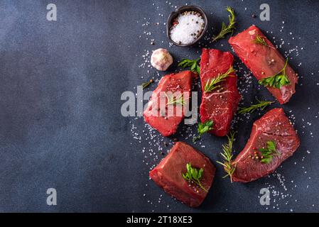 Fond de cuisson des aliments. Diverses coupes de veau frais cru, boeuf, viande rouge aux épices, romarin, sel, poivre, ail, huile d'olive, vue de dessus espace copie Banque D'Images