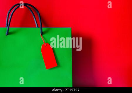 Sac en papier vert à provisions avec étiquette de prix vierge rouge sur fond rouge pour le concept de vente shopping Black Friday. Banque D'Images