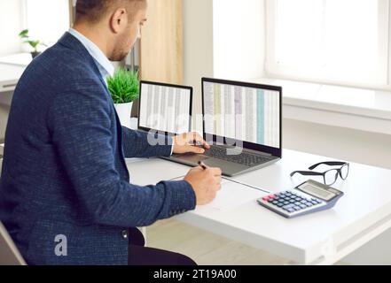Financier masculin concentré occupé travaillant dans le bureau avec des feuilles de calcul Excel et calculatrice. Banque D'Images