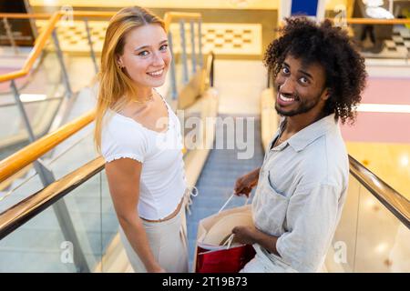 Un couple en faisant du shopping, ils sont sur les escaliers mécaniques avec leurs achats Banque D'Images