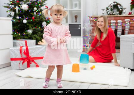 Une petite fille dans une robe rose se dresse sur la toile de fond d'un arbre de Noël Banque D'Images