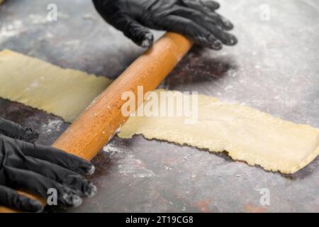 Préparation de la pâte. Confiseur déroule la pâte avec un rouleau à pâtisserie en bois Banque D'Images