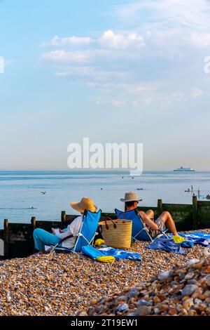 Couple sur des transats lisant et prenant un bain de soleil sur Kingsdown Beach dans le Kent Angleterre Royaume-Uni avec des bardeaux au premier plan et un grand navire à l'horizon. Banque D'Images