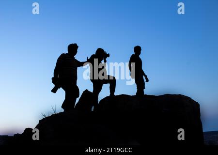 Silhouette de Groupe de photographes masculins debout ou prenant la photographie au sommet de la montagne au coucher du soleil du soir avec ciel bleu sur le fond Banque D'Images