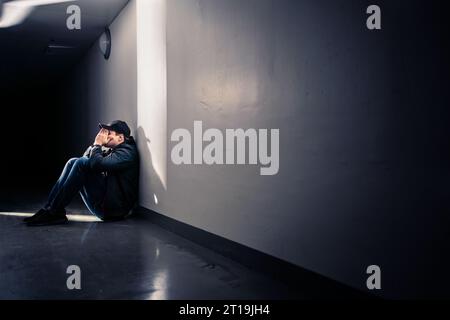 Homme triste avec traumatisme assis sur le sol. Honte, culpabilité ou tristesse. Type désespéré pleurant dans le couloir sombre. Victime de solitude ou de discrimination. Banque D'Images