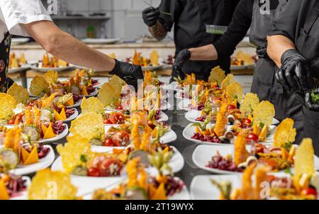 Les cuisiniers garnissent les assiettes des hors-d'œuvre dans le tableau de cuisine du restaurant Banque D'Images