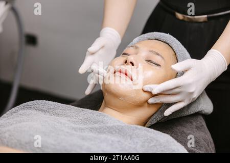 Femme massage facial traitement de la peau du visage avec la crème hydratante d'extrait de plantes d'essence naturelle dans la clinique de spa de beauté. Banque D'Images