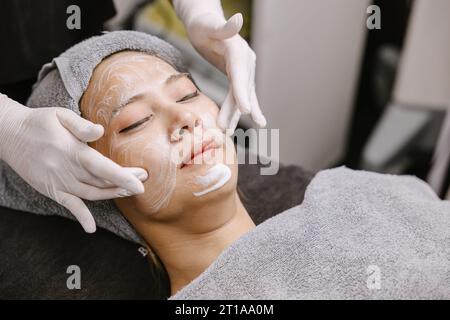 Femme massage facial traitement de la peau du visage avec la crème hydratante d'extrait de plantes d'essence naturelle dans la clinique de spa de beauté. Banque D'Images