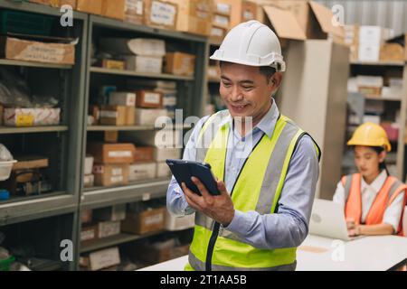Ingénieur gestionnaire d'entrepôt heureux utilisant la technologie de gestion des stocks aider à compter le contrôle des produits de stock Banque D'Images