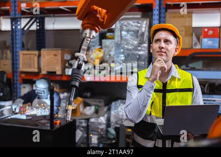 L'ingénieur caucasion mâle de service de travail fixe actionner le bras automatique de soudage de robot avec la pensée de question résolvant l'expression de problème Banque D'Images