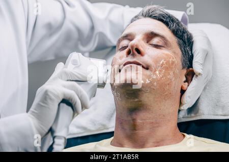 Médecin de la peau utilisant la technologie de traitement de soin du visage HIFU resurfacing avec un homme adulte pour réduire les rides et les cicatrices à la clinique anti-vieillissement Banque D'Images