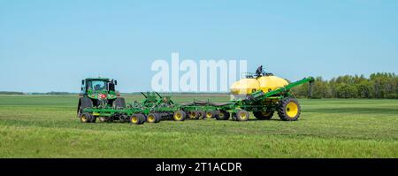 ROSEAU CO, MN - 25 MAI 2023 : un agriculteur est vu au sommet d'un réservoir jaune sur une remorque, qui le long d'un semoir pneumatique est attaché à un tracteur John Deere. Banque D'Images