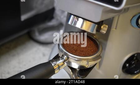 Le café moulu se déverse du moulin et tombe lentement dans le porte-filtre. Le processus de moudre des grains de café. Gros plan Banque D'Images