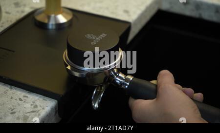 Préparation de café moulu avec tassement de café frais. Falsification de café fraîchement moulu. Un barista tient et presse la poudre de café moulu Banque D'Images