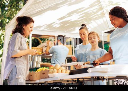 Jeune équipe de travailleurs à but non lucratif préparant un repas gratuit pour femme caucasienne sans abri pauvre. Les membres de la communauté et les bénévoles collaborent à la distribution de dons alimentaires dans un refuge. Banque D'Images
