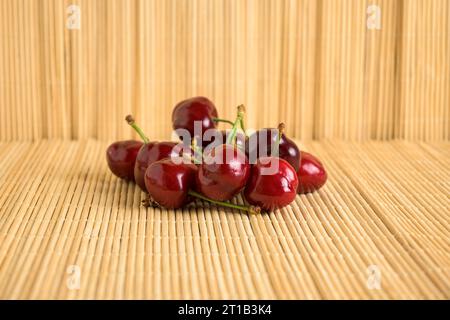 cerises rouges mûres avec tige verte prête à manger sur fond de bambou clair Banque D'Images