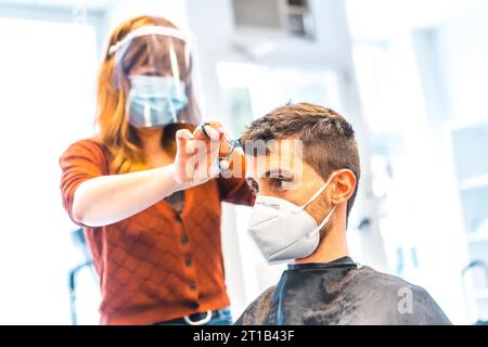 Ouverture de salons de coiffure après la pandémie de coronavirus, covid-19. Mesures de sécurité, masque facial, écran de protection, distance sociale. Banque D'Images