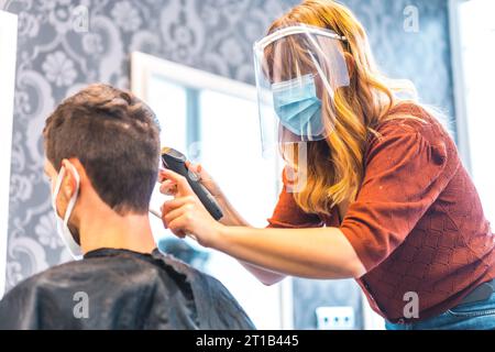 Ouverture de salons de coiffure après la pandémie de coronavirus, covid-19. Mesures de sécurité, masque facial, écran de protection, distance sociale. Coiffeur Banque D'Images