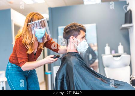 Ouverture de salons de coiffure après la pandémie de coronavirus, covid-19. Mesures de sécurité, masque facial, écran de protection, distance sociale. Coiffeur Banque D'Images