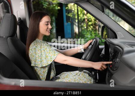 Sélection de la radio favorite. Belle jeune femme appuyant sur le bouton sur l'audio du véhicule dans la voiture Banque D'Images