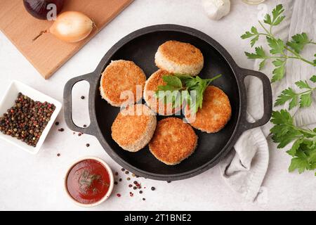 Poêle à frire avec des côtelettes de viande savoureuses et sauce sur fond blanc Banque D'Images