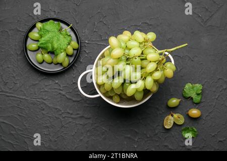 Raisins doux frais avec des feuilles dans une passoire sur fond noir Banque D'Images