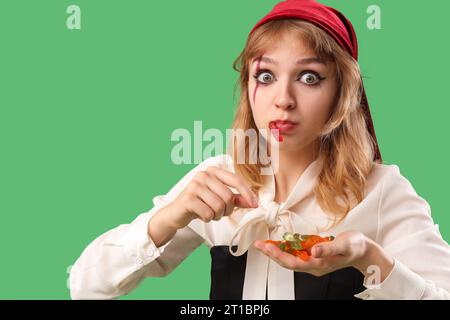 Jeune femme habillée pour Halloween comme pirate mangeant des vers de gelée sur fond vert, closeup Banque D'Images