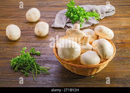 Un bol en osier rempli d'un assortiment de champignons sur une table en bois. Banque D'Images