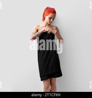 Fille aux cheveux rouges enveloppée dans une serviette noire, vue de face, photographie de produit pour la présentation. Modèle pelucheux éponge sur une femme isolée sur un ba blanc Banque D'Images