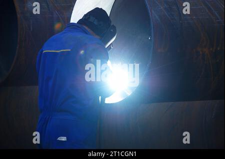 Soudeuse d'électrode industrielle avec écran facial et soudure globale bleue d'un tuyau en acier dans l'atelier. Vue arrière. Banque D'Images