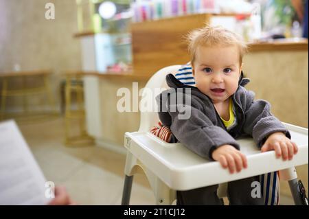 Petit garçon assis dans une chaise haute dans un café. Banque D'Images