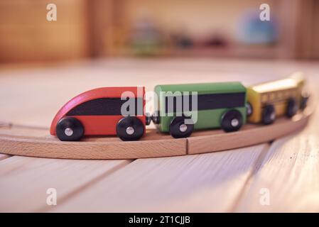 Train jouet en bois sur une piste avec chambre d'enfants défocalisée en toile de fond. Banque D'Images