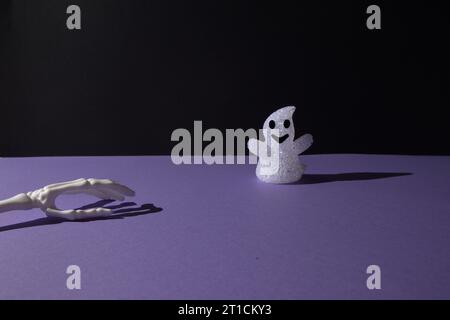 Décoration fantôme pour Helloween et os de main sur fond noir violet avec espace de copie. Concept de pose à plat minimale. Banque D'Images