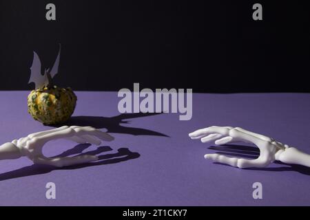 Citrouille pour Helloween et ombre de chauve-souris et os de main sur fond noir violet avec espace de copie. Concept de pose à plat minimale. Banque D'Images