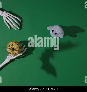 Les mains de squelette donnent à la citrouille un esprit sur fond vert, avec une ombre de chauve-souris. Concept de pose à plat minimale. Banque D'Images