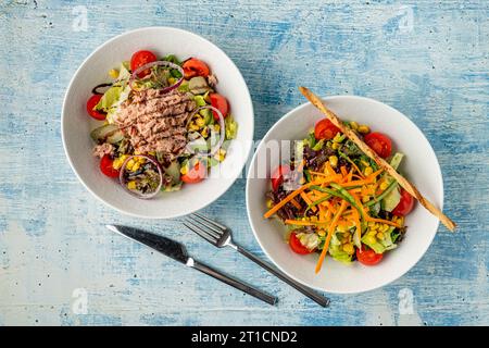 Salade de thon, carottes, tomates, maïs et beaucoup de légumes verts sur des assiettes en porcelaine blanche Banque D'Images