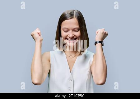 Jeune femme joyeuse serrant ses poings sur fond gris Banque D'Images