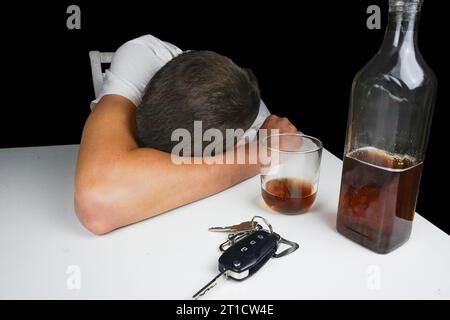 Clés de voiture et alcool sur la table. Homme ivre dormant sur la table avec bouteille de whisky et boisson. Alcoolisme. Ne conduis pas quand tu es saoul. Banque D'Images