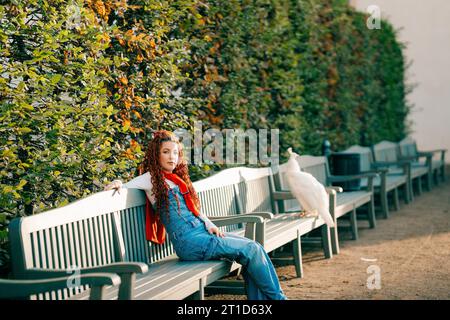 Jeune femme assise sur un banc à côté d'un paon dans un parc à Prague Banque D'Images