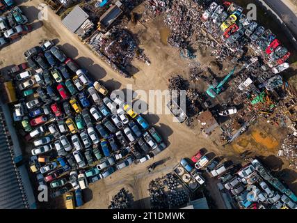 vue aérienne d'une décharge de voiture, où une machine est vue séparant les vieilles voitures en ferraille. La collection massive de voitures abandonnées et la machinerie lourde nous Banque D'Images