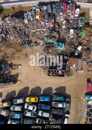 vue aérienne d'une décharge de voiture, où une machine est vue séparant les vieilles voitures en ferraille. La collection massive de voitures abandonnées et la machinerie lourde nous Banque D'Images