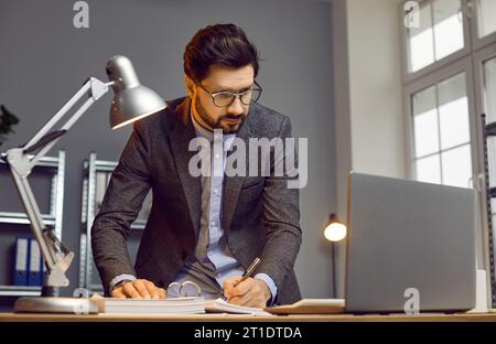 Bel homme d'affaires occupé travaillant sur un certain projet dans le bureau moderne Banque D'Images