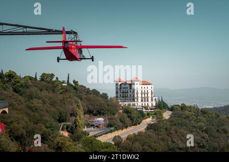 Carrousel sous la forme d'un avion volant rouge au parc d'attractions Tibidabo à Barcelone. Gran Hotel la Florida en arrière-plan Banque D'Images