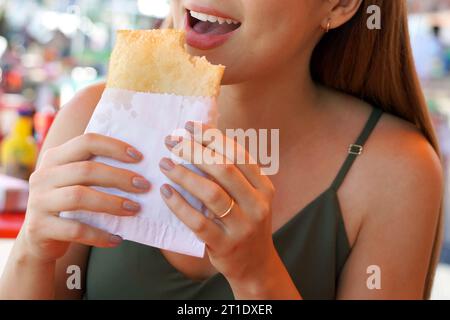 Heureuse jeune femme mangeant pastel de feira une pâtisserie frite farcie brésilienne traditionnelle Banque D'Images