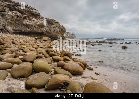 Capturée sous un angle bas, l'image montre une plage rocheuse escarpée menant à un affleurement majestueux au bord de l'eau Banque D'Images