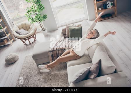 Photo vue de dessus de l'adorable dame senior excitée habillée cardigan blanc s'étirant profitant de la salle de la maison intérieure du matin Banque D'Images