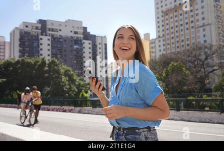 Heureuse fille brésilienne souriante tenant smartphone sur l'autoroute Minhocao dimanche à Sao Paulo, Brésil Banque D'Images